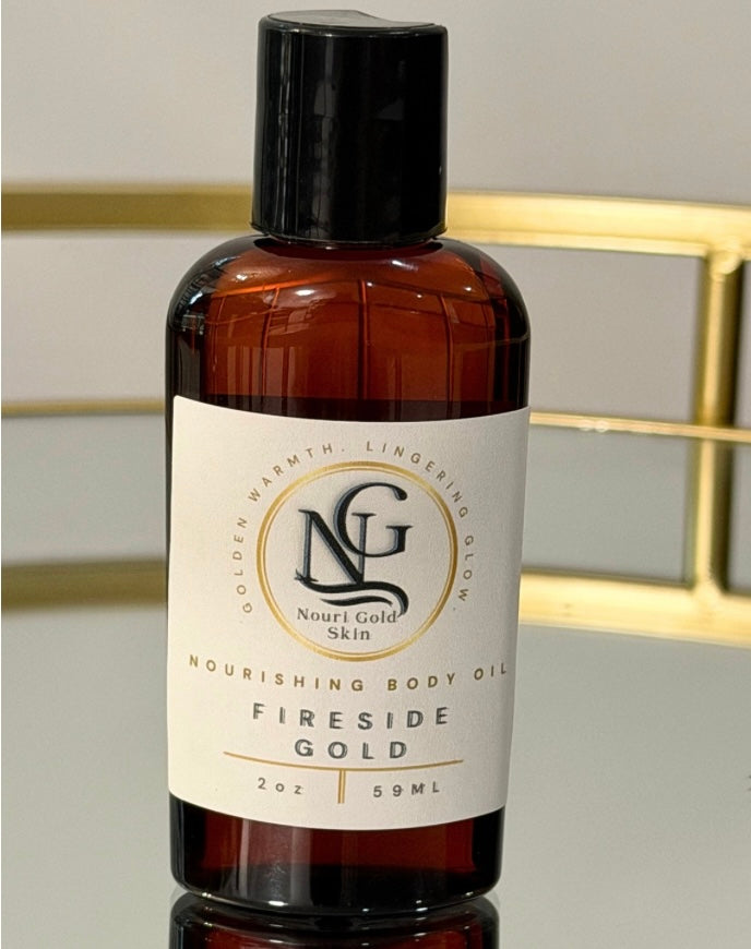 An amber plastic bottle of Nourish Gold Skin 'Fireside Gold' nourishing body oil with a black cap and white label, set against a softly blurred background with gold accents.